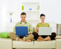 Young couple sitting on sofa, using laptops